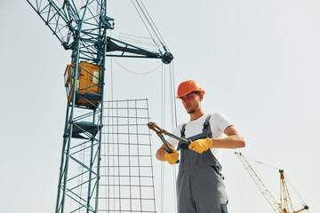 Crane is at background. Young construction worker in uniform is busy at the unfinished building