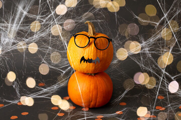 halloween and holiday concept - halloween pumpkins with glasses, bat and spiderweb over lights on...
