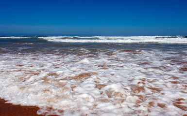 Sandy beach with long waves and white foam on the southern coast of the ocean.