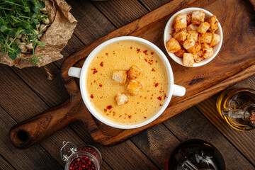 Yellow chicken cream soup with croutons in a white bowl on rustic background