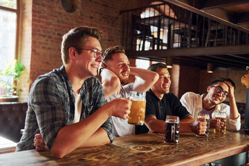 With beer in hands. People in casual clothes sitting in the pub