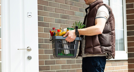 The guy delivers the basket full of groceries to the door of the house. Online shopping. © SkyLine