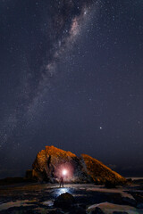 Milkway sky over Currumbin Rock, Gold Coast with person holding light.