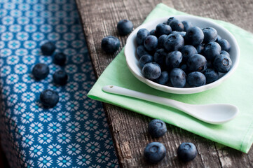 Blueberries on a white plate with a white spoon on a wooden background