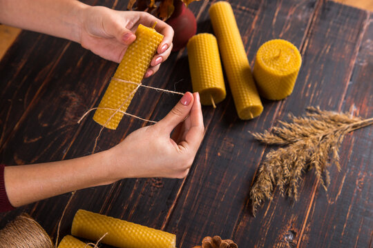 Women's hands make handmade candles of natural wax with texture of honeycomb bees, on a wooden table.
