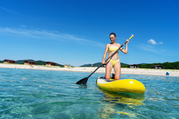 Woman stand up on paddle board in sea. Big yellow board in turquoise water.
