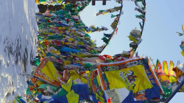 Lots of colorful prayer flags with tibetan mantras hanging out in wind near yellow stupa at temple complex Rinpoche Bagsha in snowy Siberia at cold winter, vertical image