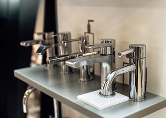 Group of modern stylish water taps for bathroom in showroom. Rows of new faucets in plumbing shop, closeup. Selective focus
