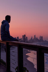 A person sitting on the guard rail on Miami Lookout, over looking the Gold Coast cityscape at dusk.