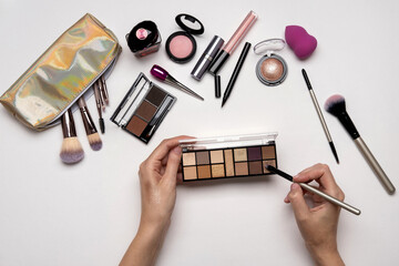 Top view of woman holding eyeshadow on hands over white table with cosmetic products. Decorative cosmetics and makeup brushes