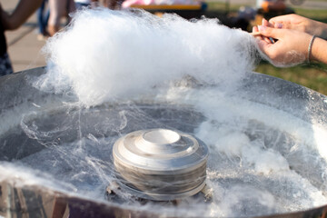 Close-up of the hands of a man who makes cotton candy. Wooden stick will wind the threads of the sweet cobweb. Sweet cloud and melted treat machine. Concept of cooking street food and carnival yummy.