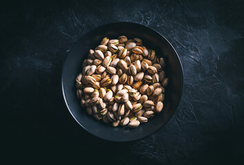Pistachios in a dark bowl on a dark table. Ready to eat nuts. Energy food. 