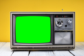 An old vintage 1970s TV with a green screen for adding video stands on a wooden table against a...
