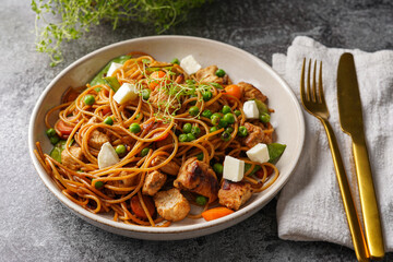 Italian pasta spaghetti with chicken, green beans and cheese mozzarella and fresh thyme in light grey bowl on grey concrete surface, golden silverware and beige colored napkin