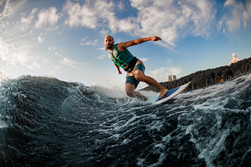 adult athletic man in turquoise life jacket rides down the wave on a wakesurf