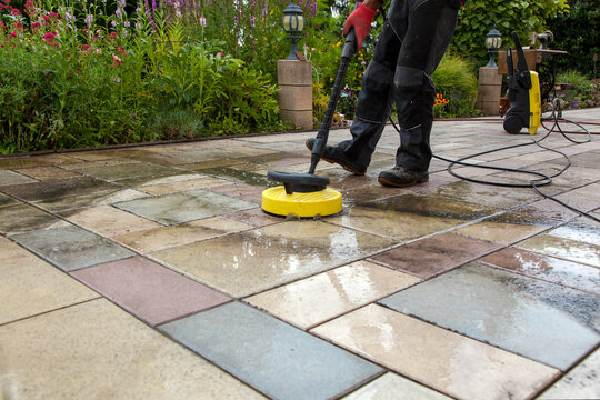 Cleaning stone slabs on patio with the high-pressure cleaner. Person worker cleaning the outdoors floor.  