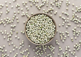 Legumes in bowl and scattered in the background, green peas in a plate on a gray background, top view