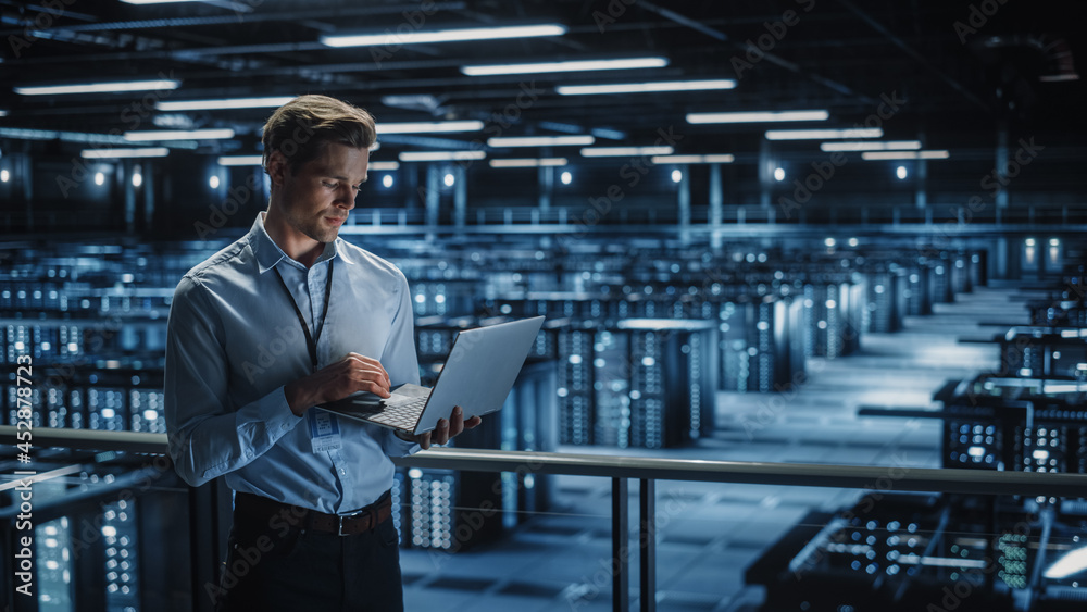 Poster Portrait of IT Specialist Uses Laptop in Data Center. Server Farm Cloud Computing Facility with Male Maintenance Administrator Working. Cyber Security and Network Protection.