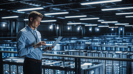 Portrait of IT Specialist Uses Laptop in Data Center. Server Farm Cloud Computing Facility with Male Maintenance Administrator Working. Cyber Security and Network Protection.