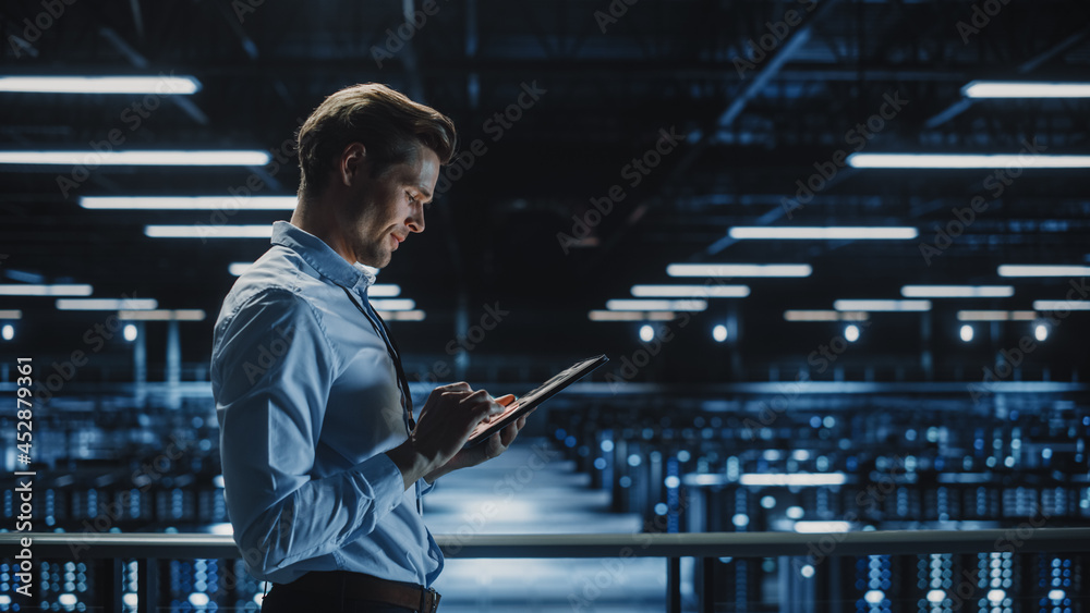 Poster Handsome Smiling IT Specialist Using Tablet Computer in Data Center. Succesful Businessman and e-Business Entrepreneur Overlooking Server Farm Cloud Computing Facility.