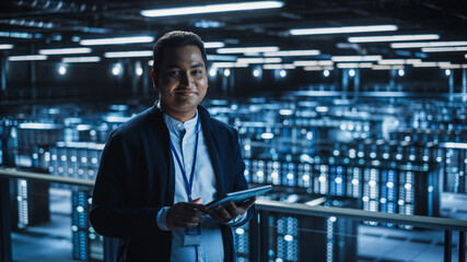 Handsome Smiling IT Specialist Using Tablet Computer in Data Center, Looking at Camera. Succesful...