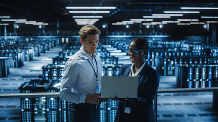 Data Center Female System Administrator and Male IT Specialist talk, Use Laptop. Information Technology Engineers work on Cyber Security Network Protection in Cloud Computing Server Farm.