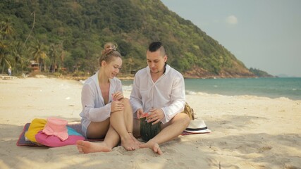 The cheerful love couple holding and eating slices of watermelon on tropical sand beach sea. Romantic lovers two people caucasian spend summer weekend in outdoor. Hat, backpack white shirt beachwear.