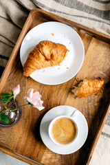 Fresh coffee with croissant on a wooden tray with a pink tulip in a glass vase.