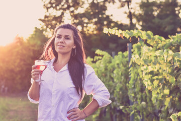Fototapeta premium Young beautiful Happy smiling Brunette Woman walking at Vineyard with a glass of rose wine.Wine tourism