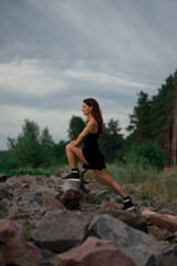 Woman in black sport suit is doing fitness working out outside near beautiful river and stones