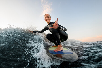 smiling woman sits on wakesurf board and rides the wave and touches the waves with one hand - Powered by Adobe