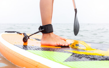 Stand up paddle board on a sea lake, close-up of legs with a safety rope. Person on a SUP. Paddle Boarding, water sports. Active healthy lifestyle, digital detox. Traveling, summer vacation.