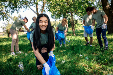 Portrait of young woman with garbage bags cleaning city park with friends.