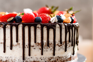 Beautiful cake with fresh berries and chocolate drops on a cake stand on a white wooden background. Space for text. High quality photo