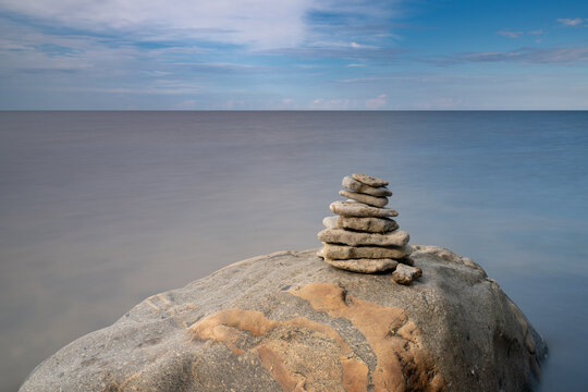 meditative rock cairn on top of a boulder with long exposure ocean and sky in the background