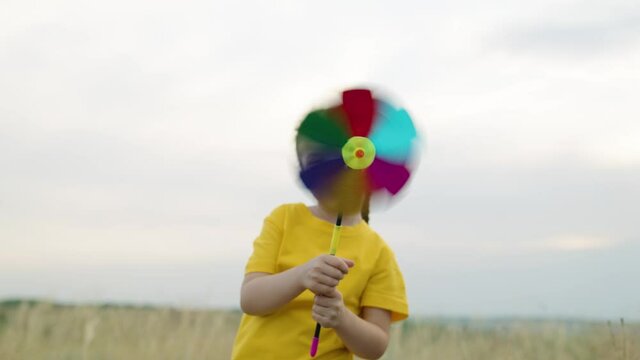 Happy child kid playing fun windmill turntable outdoors. Family holiday. Little girl plays with a toy multicolored turntable in her hand in autumn in park. Happy family resting on a weekend in nature.