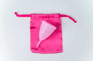 Pink menstrual cup and silk bag on a white background. Copy space