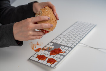 A faceless woman is eating a burger and dripping ketchup on the keyboard