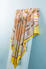 Subject photo of bright scarf with colorful fashion design. Stylish silk headkerchief is hanging on the white board.  