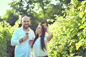 Fototapeta premium Portrait of a smiling happy couple kissing in a Vineyard toasting wine. Beautiful brunette woman and bearded muscular man spending time together