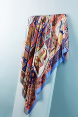 Subject photo of bright scarf with colorful ethnic design. Stylish silk headkerchief is hanging on the white board.  