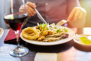 close up of a man eating fried fish at a restaurant. variety fish dish