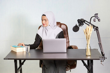 muslim business woman looking down at the books during working on laptop computer in her desk