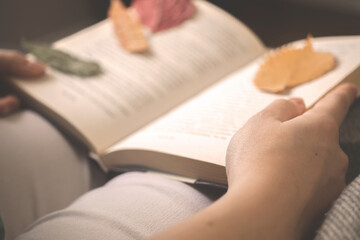 Girl reading old book in cozy autumn days. Book with autumn leaves warm toned background