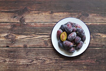 Fresh plums in a vintage bowl on an old wooden table. Flat layot, copy space 