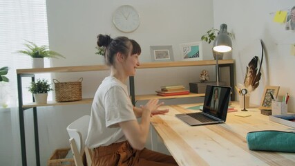 Young woman sitting at desk, smiling and chatting on online video call on laptop while staying at home