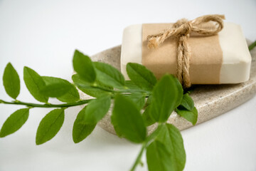 Close up of organic natural soap bar wrapped in craft paper lays on tray with aromatic herbs.