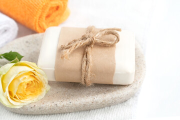 Fototapeta na wymiar Piece of organic soap wrapped in craft paper on tray with fresh yellow rose and colorful rolled towels.