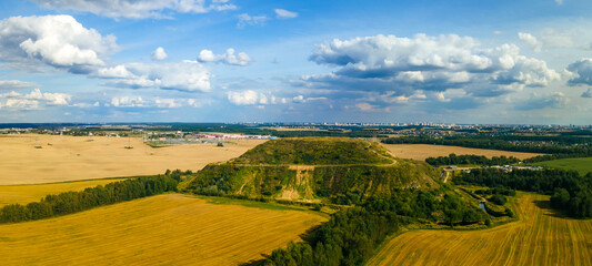 Closed city dump. Restoration of the territory. Landscaping of a large hill of garbage. In the background is a metropolis and a blue sky with clouds. Ecological problem.