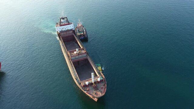 A tug pulls a cargo ship in the port. View from above. Shooting from a drone. 